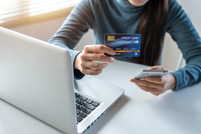 person holding their credit card in front of their laptop before making an online payment